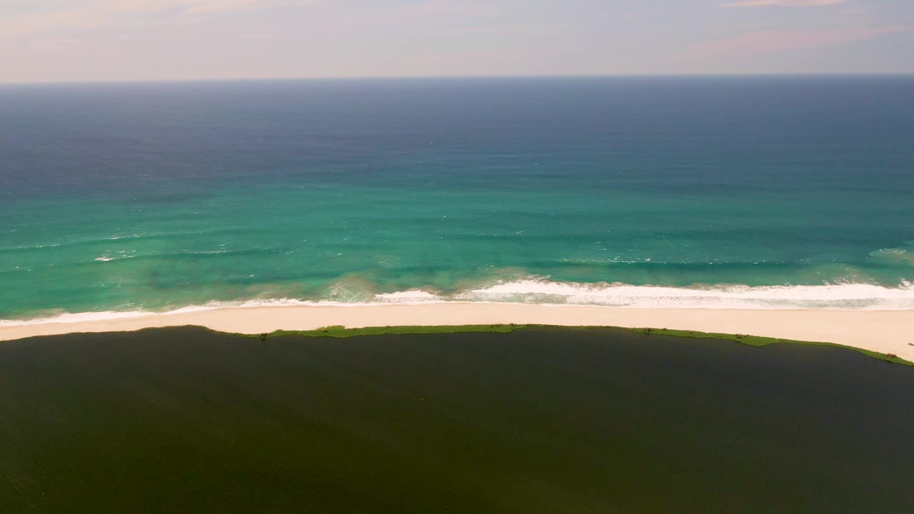 At two seconds, white foam breaks more distinctly along the San Jose del Cabo beach below turquoise and deep blue water, with no visible people.