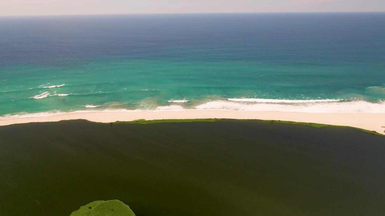 Coastal dunes below a bright beach with small whitecaps offshore.