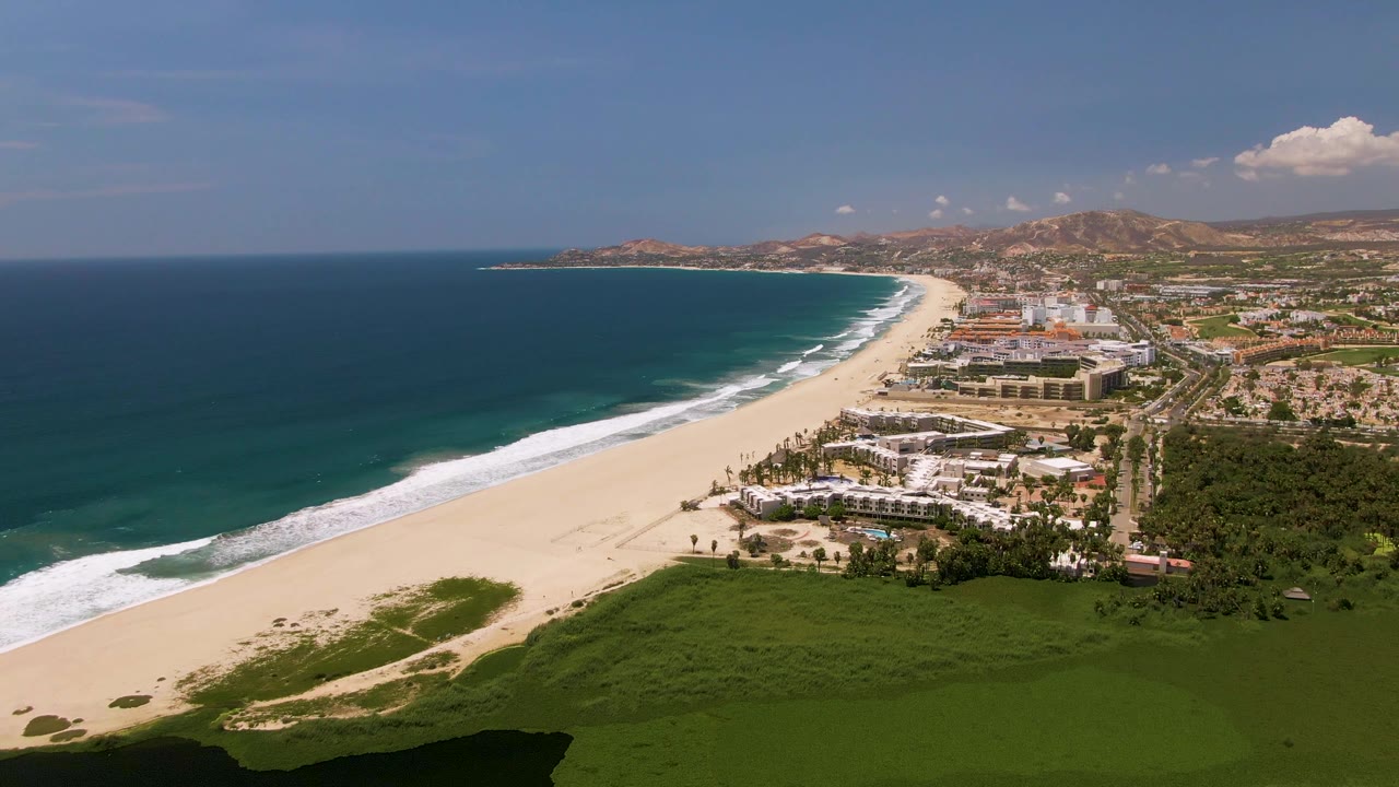 Elevated shoreline view with ocean, beach, vegetation, buildings, and mountains in the distance.