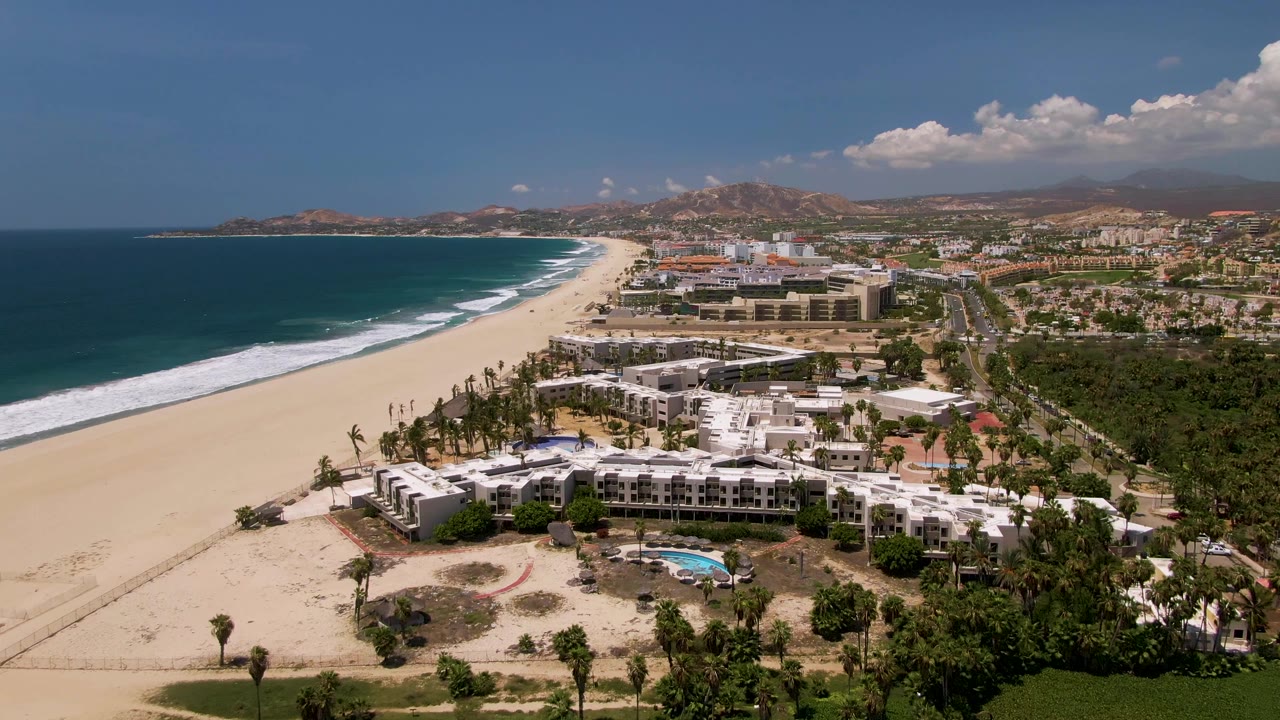 Aerial view of beach resort, ocean, pool, palms, and inland hills