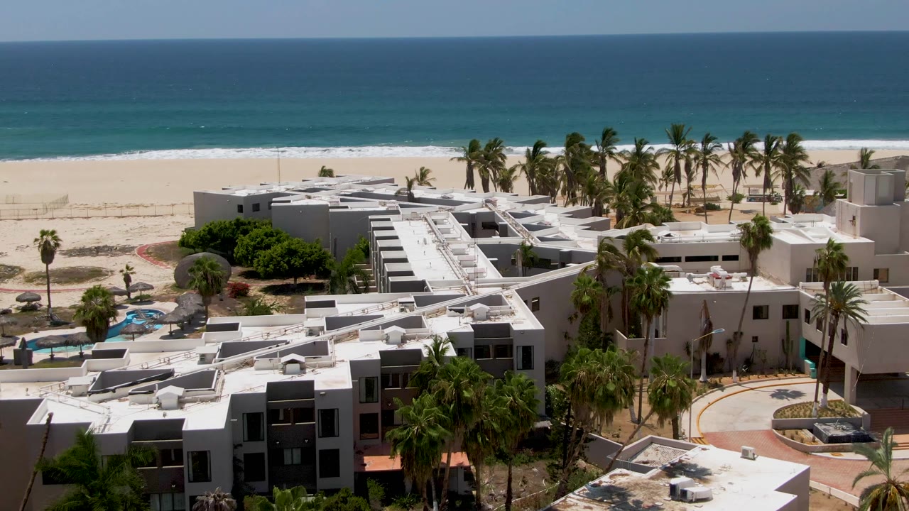 White beachfront buildings and palms seen from above with ocean behind them.