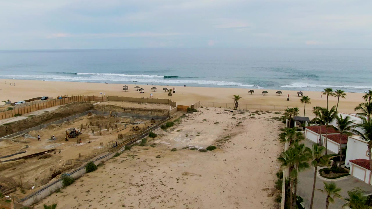 Beach construction area with palm trees and umbrellas facing the ocean.