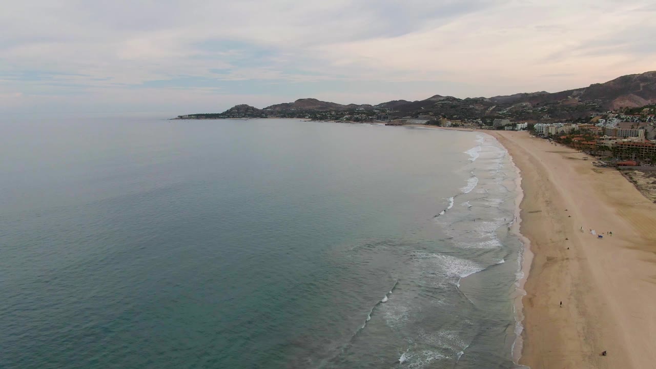 Drone view of gentle surf running along a long sandy shore.