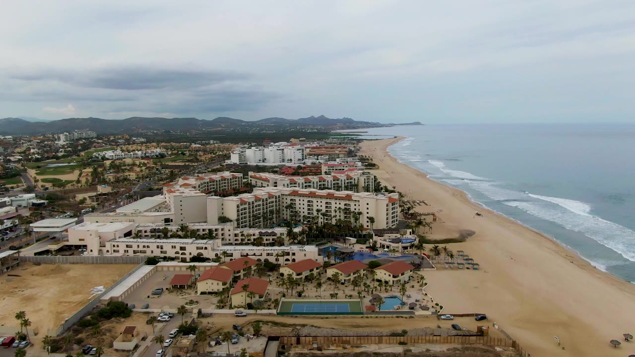 Aerial view of resort buildings beside a sandy beach and ocean waves.