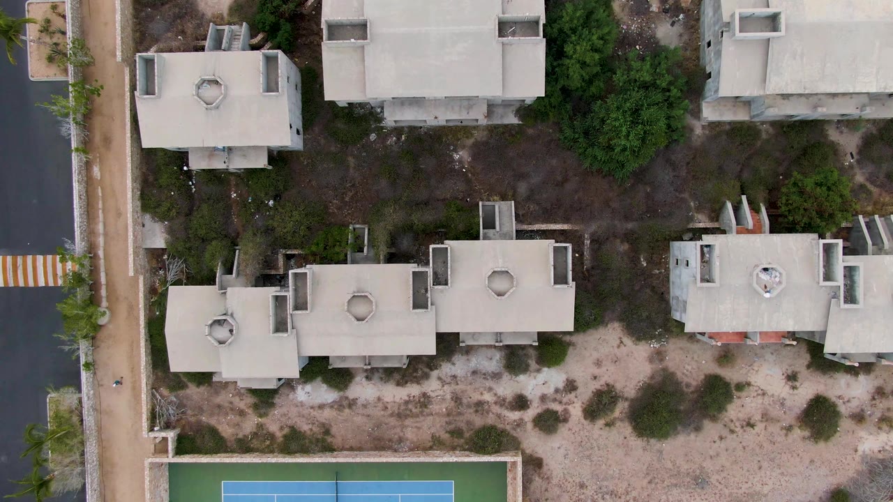 Straight-down drone view of homes and a tennis court corner in a residential area.