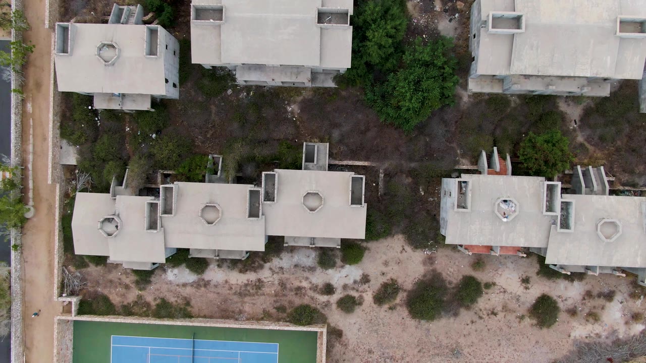 Overhead shot of residential rooftops with a blue tennis court along the bottom.
