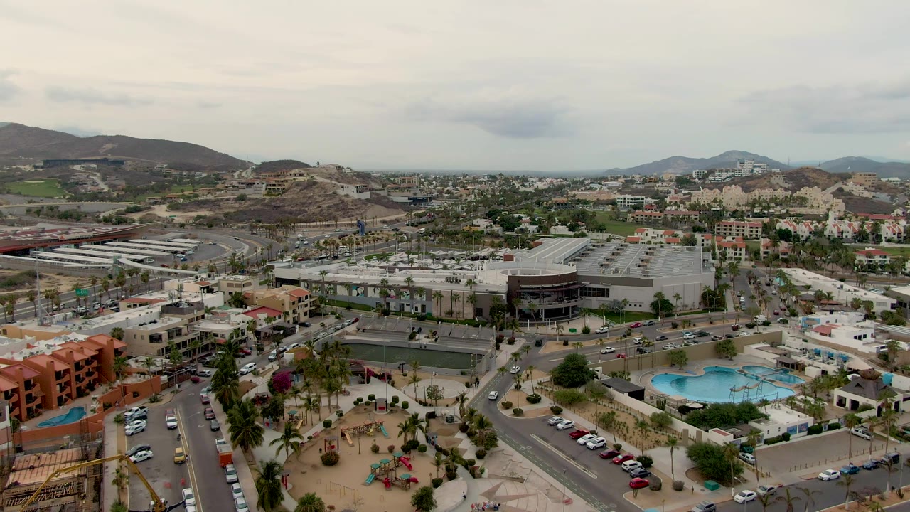 High aerial view of a commercial and residential district with roads, cars, palms, pool, and hills.