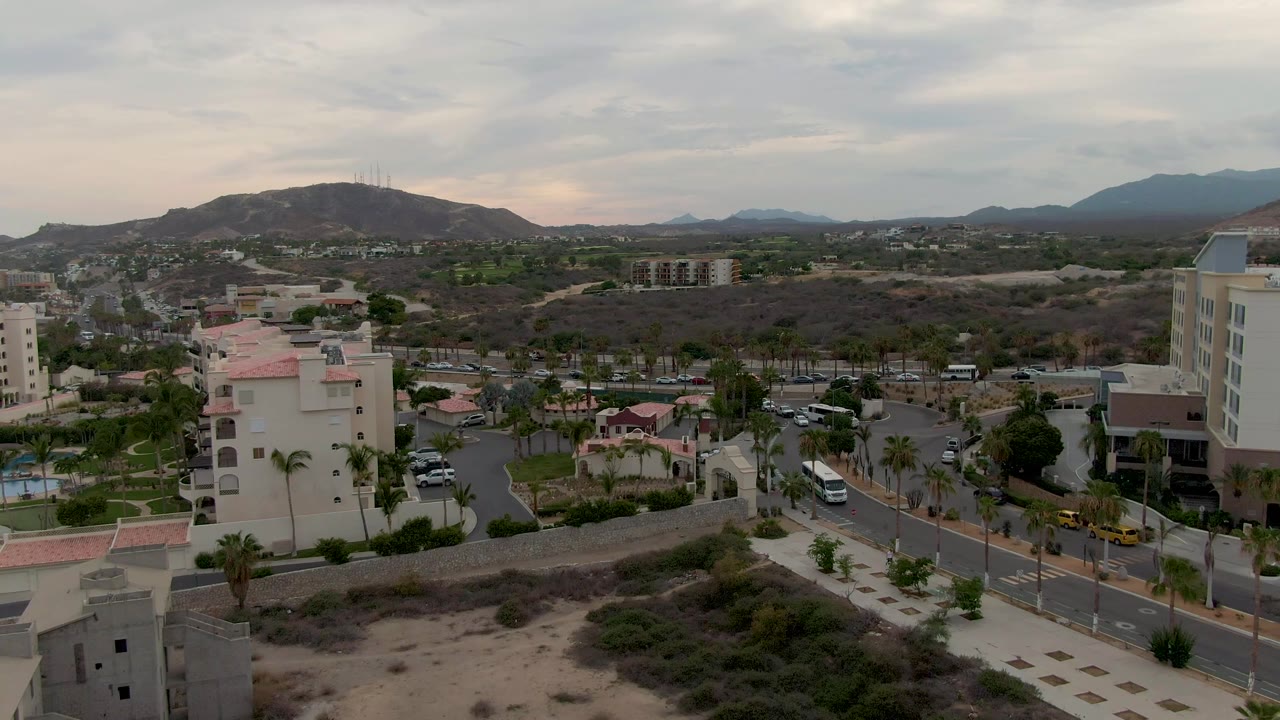 Wide elevated city edge with road traffic, palms, buildings, and mountains.