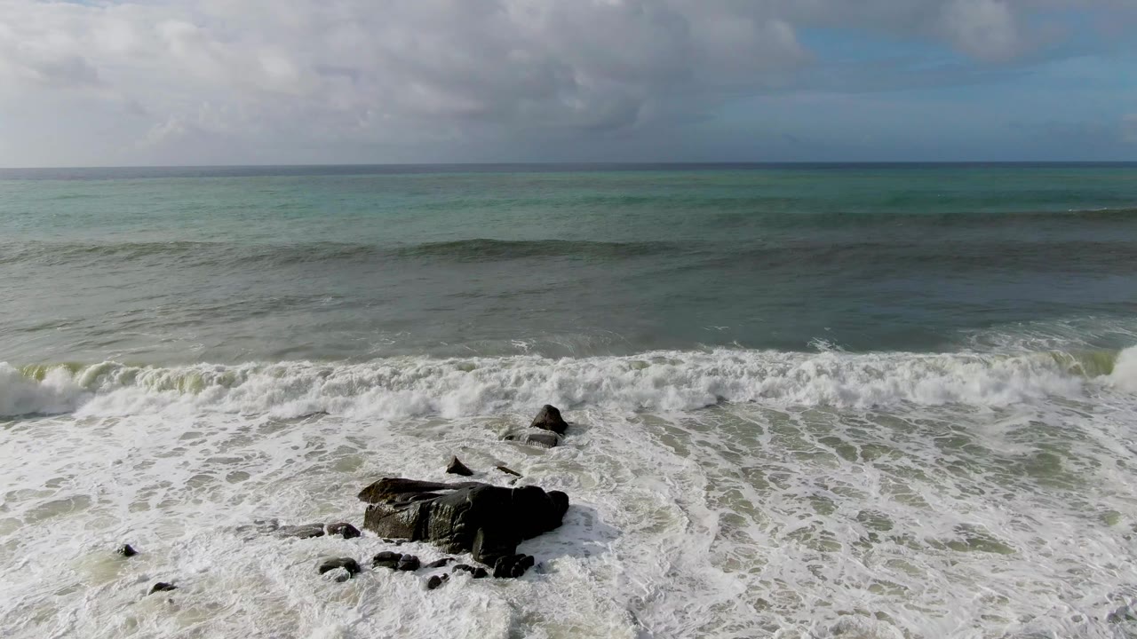 Receding foamy surf around a large dark rock.