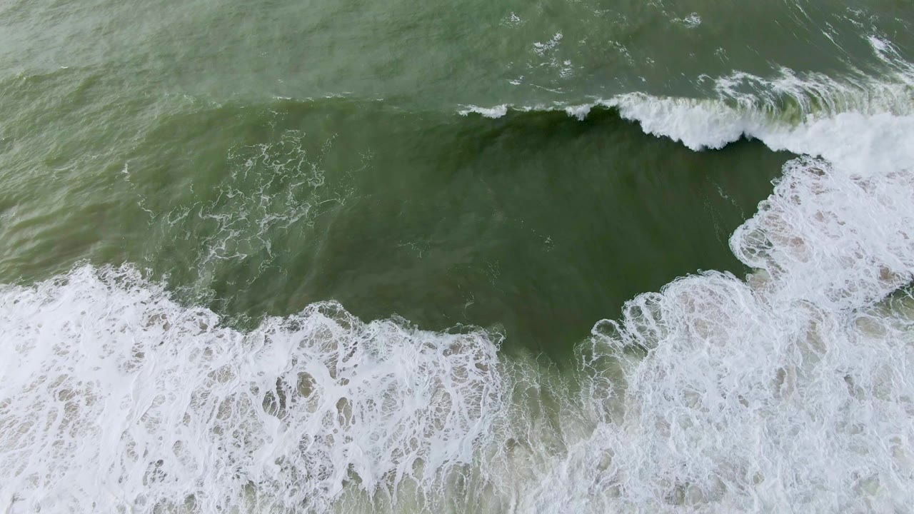 Overhead view in Punta Gorda, Baja California Sur, showing a green ocean wave starting to curl with white foam spreading along the lower edge and no visible people.
