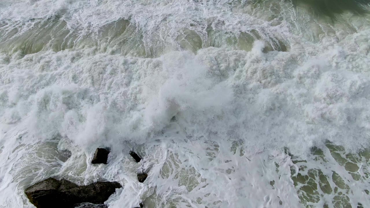 White surf washing over dark rocks in green-gray ocean water.