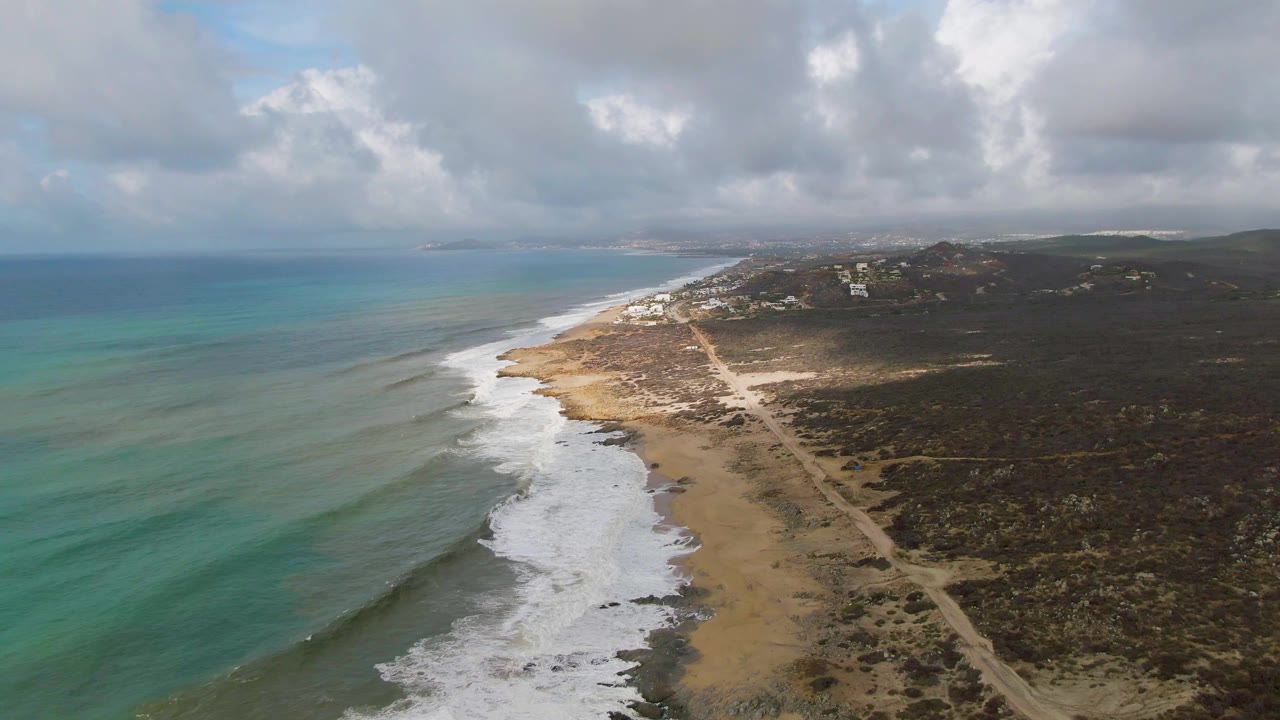 Aerial coastline with turquoise sea, surf foam, beach road, and scrub
