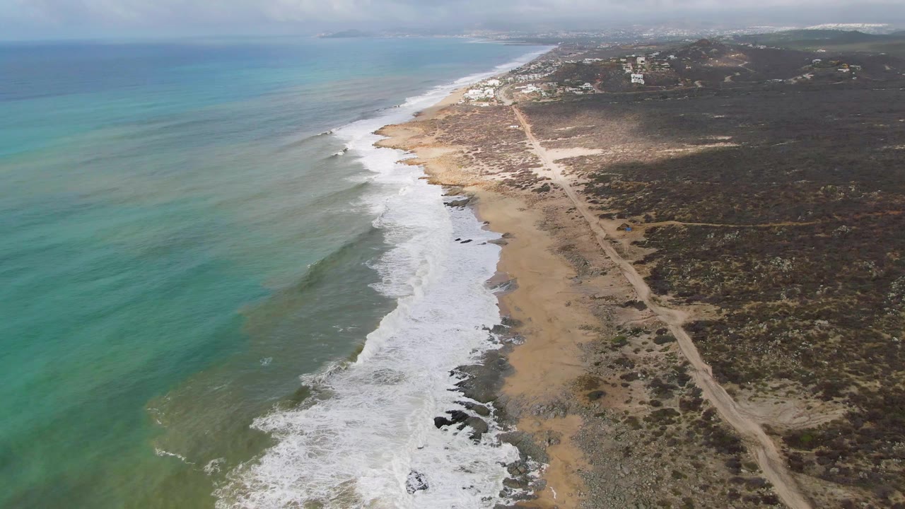 Aerial coastal frame with whitewater on the beach and turquoise water offshore.