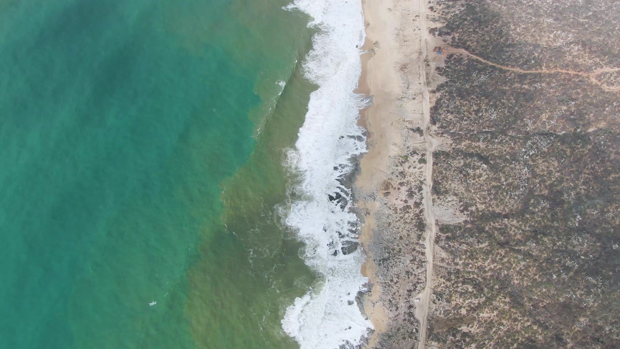 Ocean waves washing onto a narrow beach from above