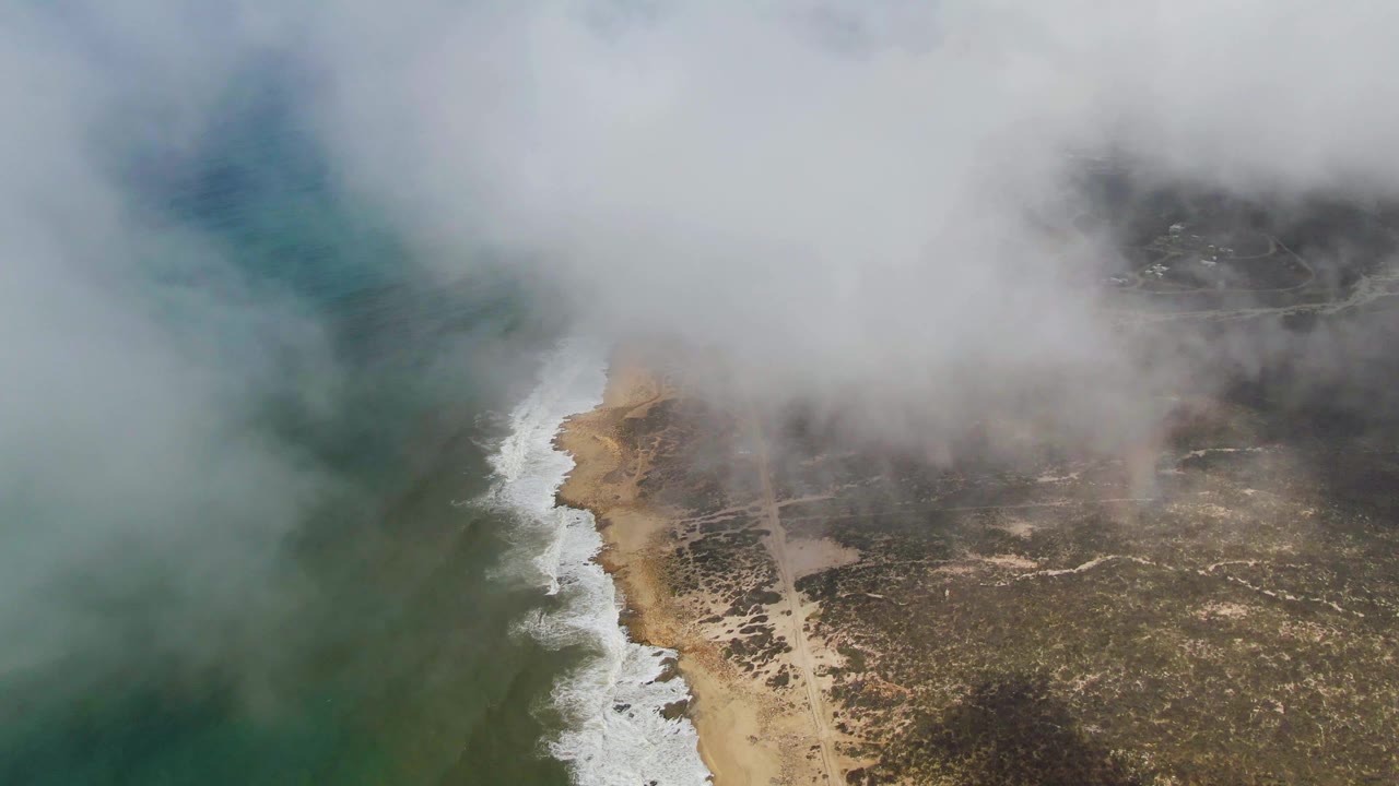 Aerial view of fog covering the ocean and sandy Punta Gorda shoreline in Baja California Sur, with surf along the beach and no visible people.