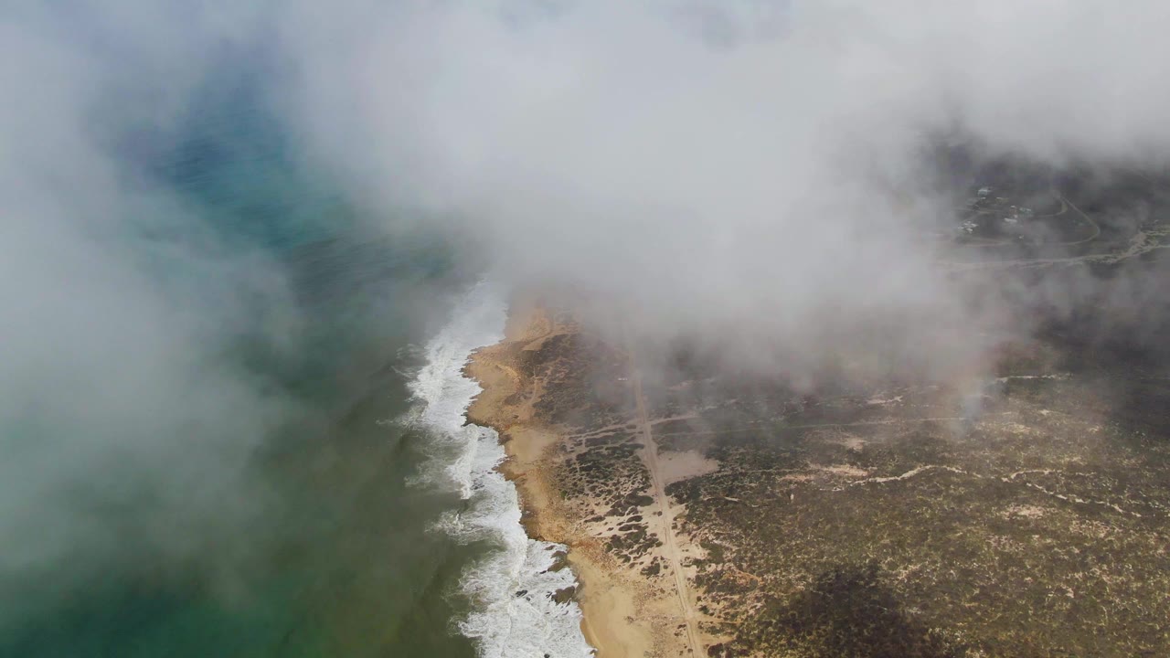 Fog hangs over green-blue ocean beside the sandy Punta Gorda coast, with white waves marking the shoreline and no visible people.