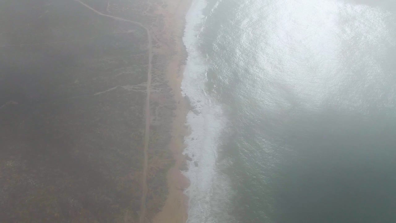 At 0:03, the surf line sits close to the sandy beach as the Punta Gorda road and surrounding scrub appear darker beneath thick coastal haze, with no visible people.