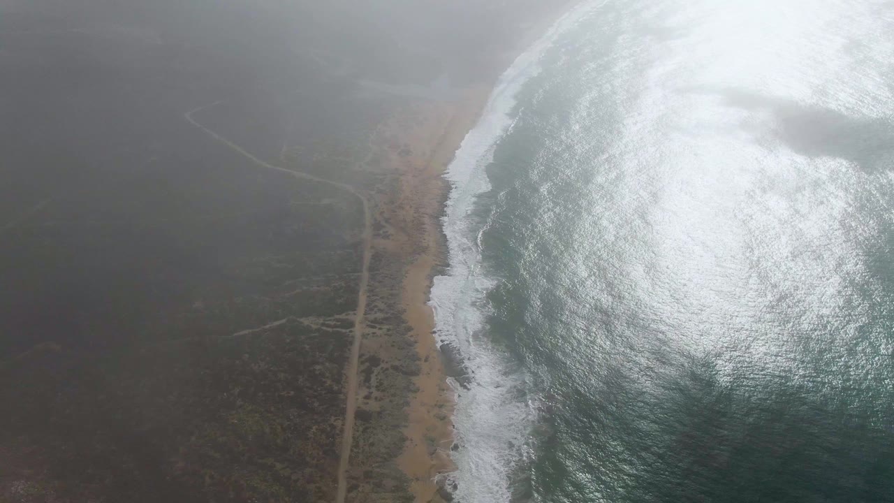 Fog clearing over sandy shoreline and coastal road from above