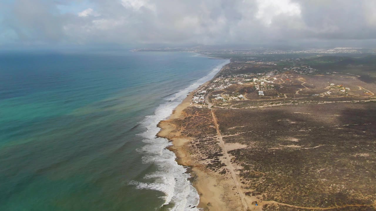 Aerial view down a long sandy shoreline with turquoise water and cloud shadows.