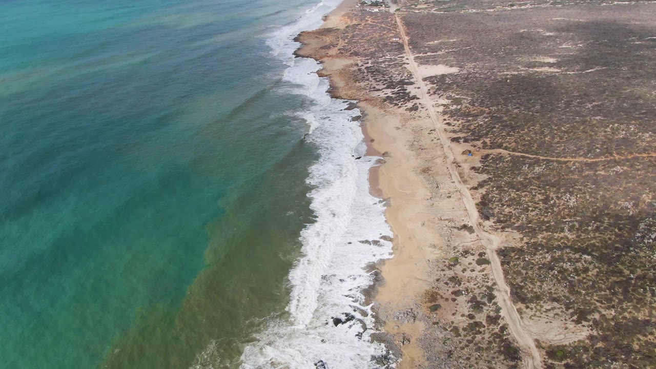 At two seconds, green-blue water fills more of the left frame while white surf curls onto the sandy Punta Gordo shore and the road stays visible through dry inland terrain, with no visible people.