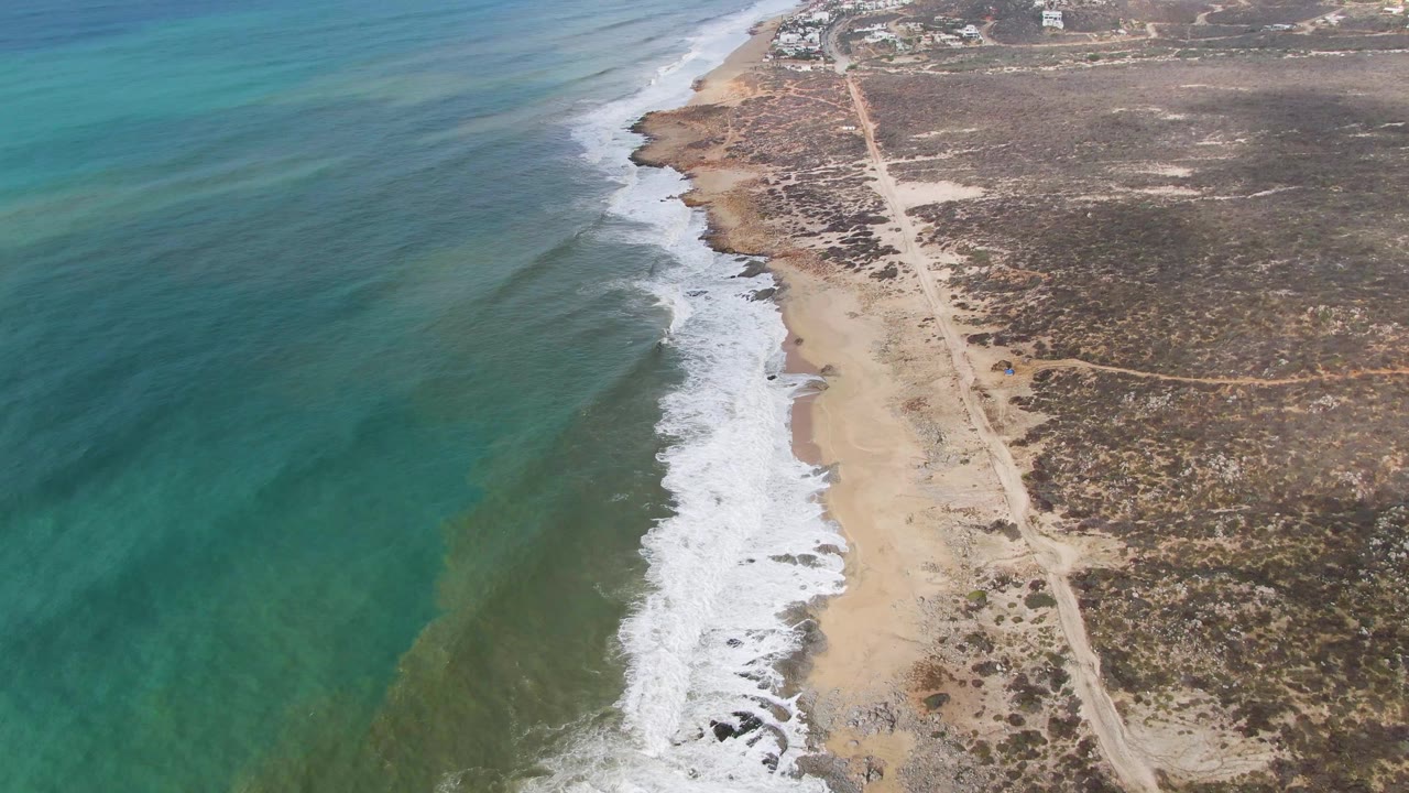 At three seconds, the drone view holds the beach and road alignment, with white surf stacked along the sand and broad turquoise water to the left near Punta Gordo, with no visible people.