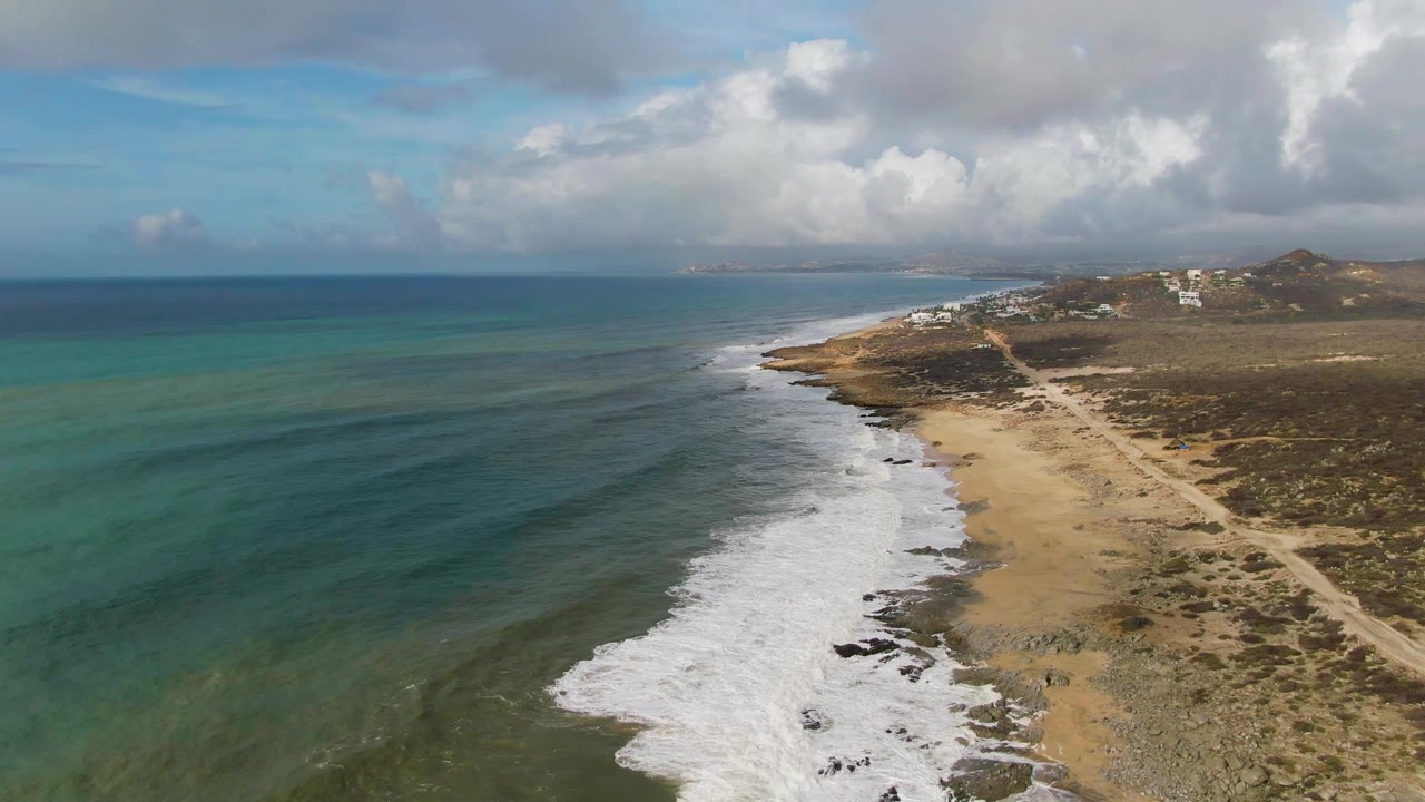Drone perspective over turquoise water and white surf beside a sandy coast