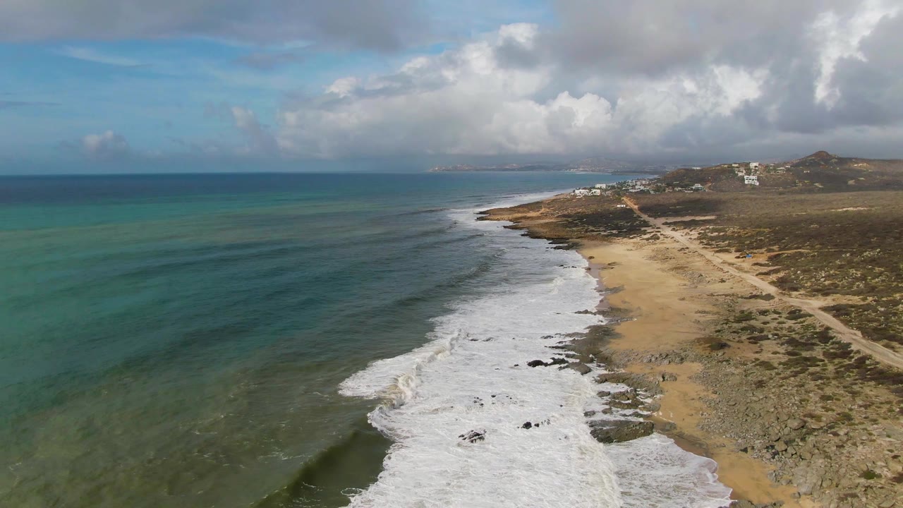At 0:01, the Punta Gorda shoreline remains in a high aerial view as white foam advances along the sand and rocks, with open water to the left and no visible people.