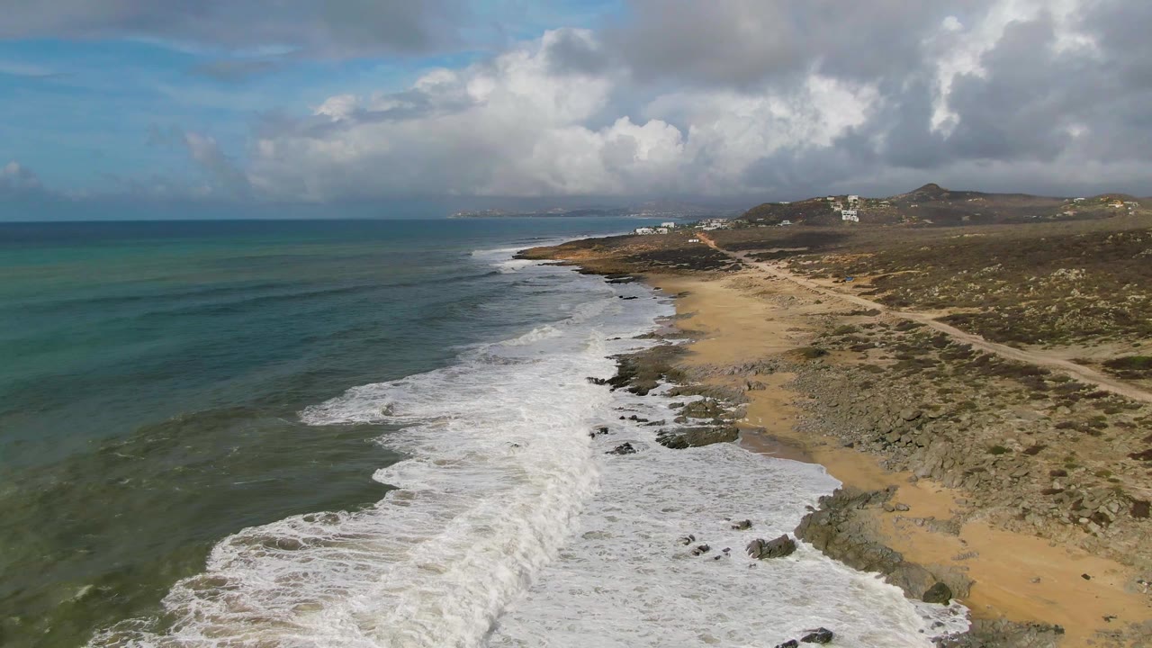Foamy surf advances along a rocky beach with open ocean to the left.
