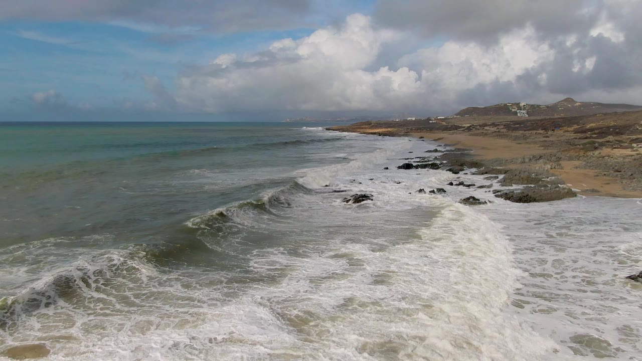 Ocean swell curling beside a rocky shoreline under clouds
