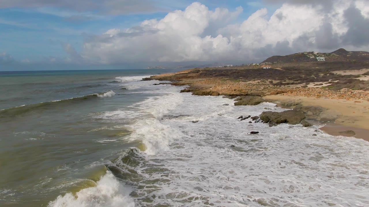 Foamy surf spreads along a rocky beach below cloudy sky