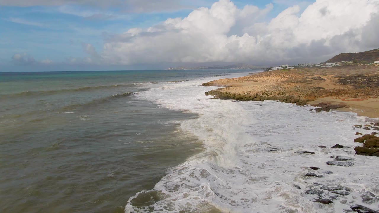 Aerial coastal view with surf washing along rocks and sand.