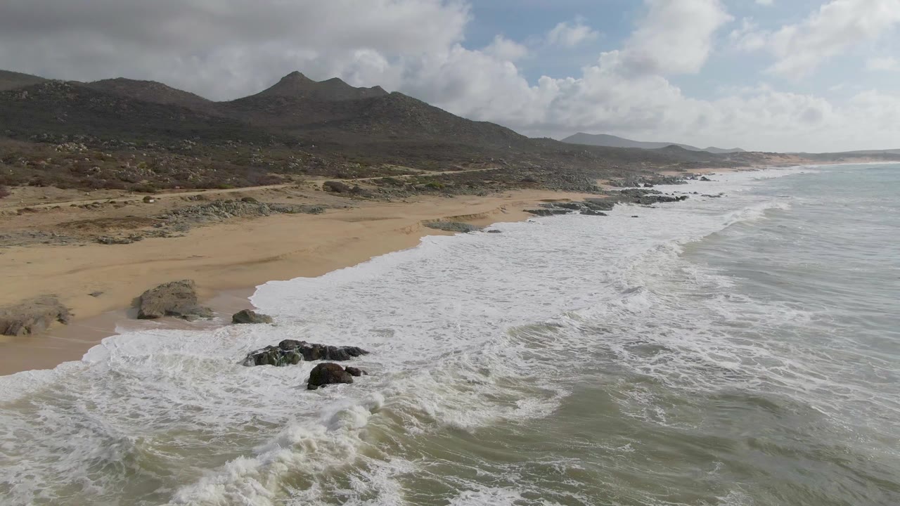 Aerial coastline view with surf breaking beside a large beach rock.