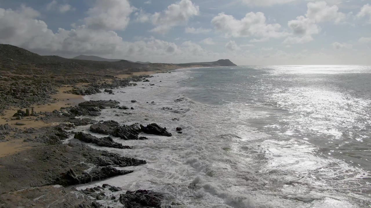 Rocky beach foreground with waves receding into bright open water.