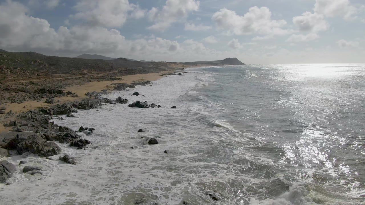 Aerial view of waves breaking along a rocky beach under clouds
