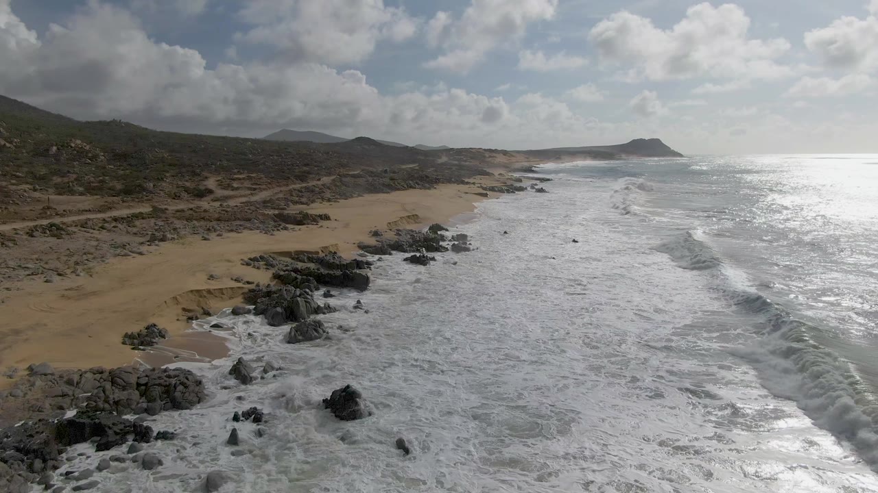 Aerial coastline view with waves pushing onto a sandy rocky beach.