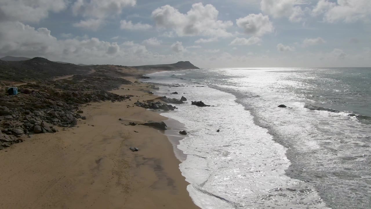 Aerial view of waves washing onto a sandy beach beside rocky outcrops.