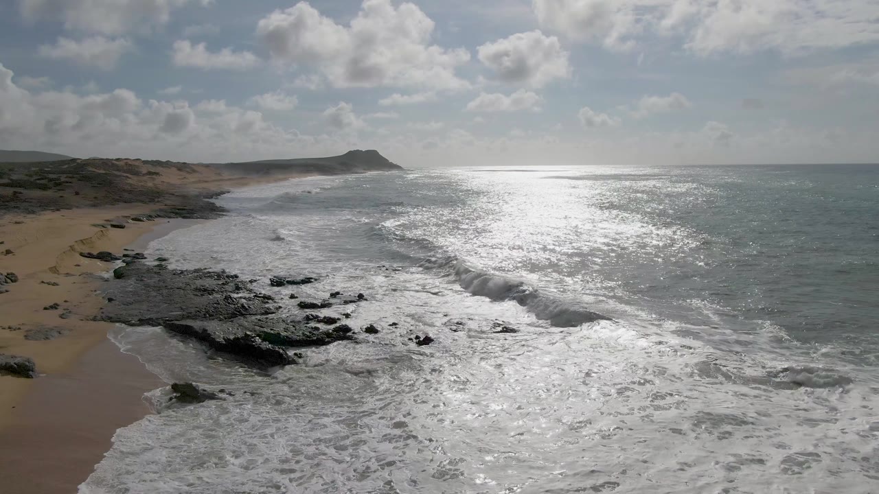 Breaking wave beside black rocks and sandy shoreline