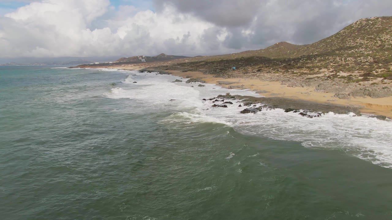 Midway through the clip, foam fans across dark rocks near the Punta Gorda shore while the foreground water remains textured by small ripples and no people are visible.