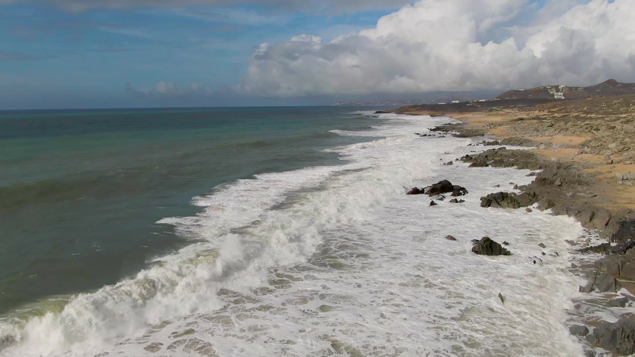White surf rolls toward rocks on a dry coastal shoreline