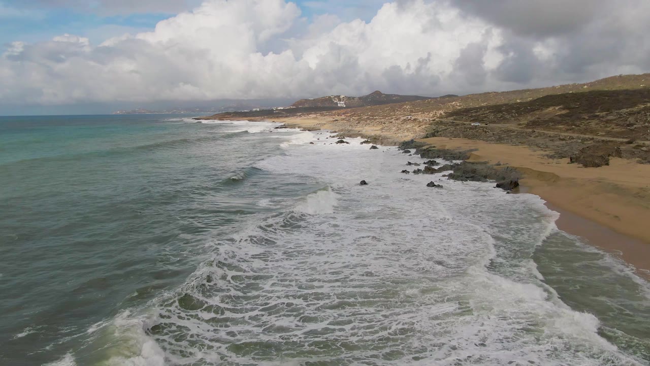 Aerial view of waves breaking along a sandy and rocky coastline.