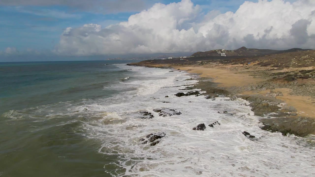 Aerial view at Punta Gorda, East Cape, Baja California Sur, with white surf spreading over dark rocks beside a sandy beach and no visible people.