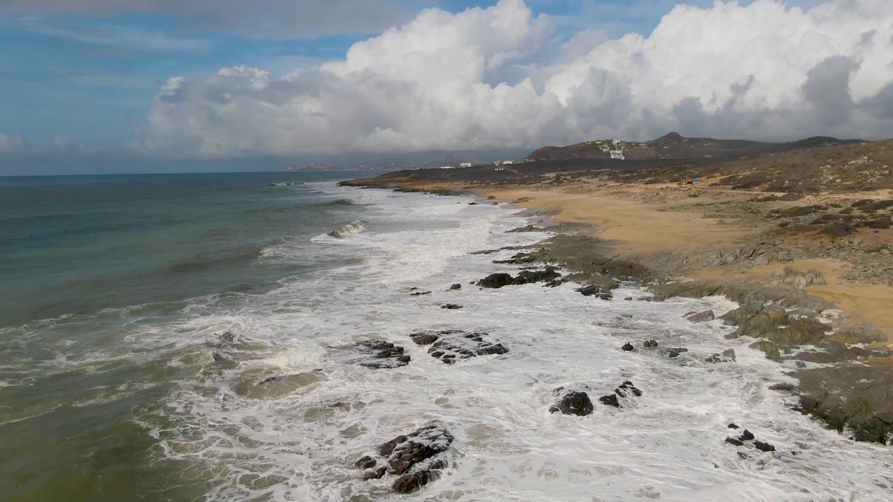 Foamy waves washing over rocks beside a long sandy beach