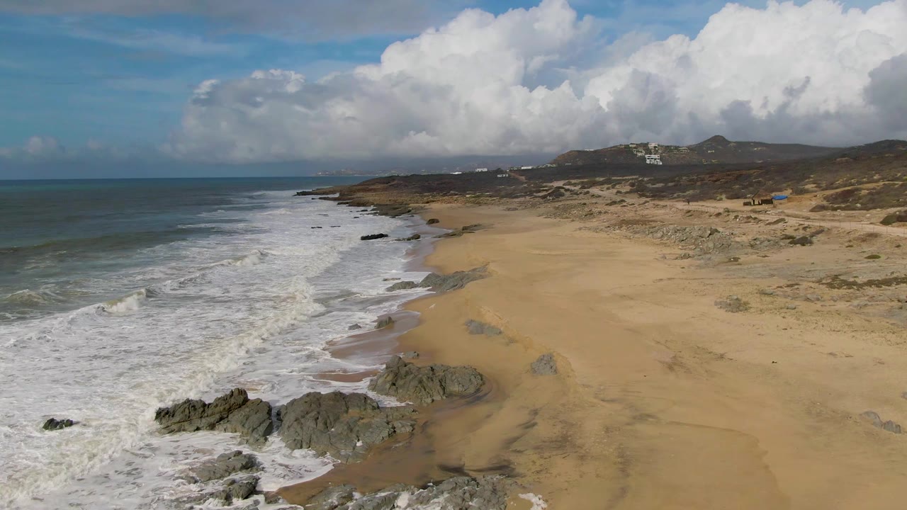 Surf washes around shoreline rocks beside a wide sandy beach.