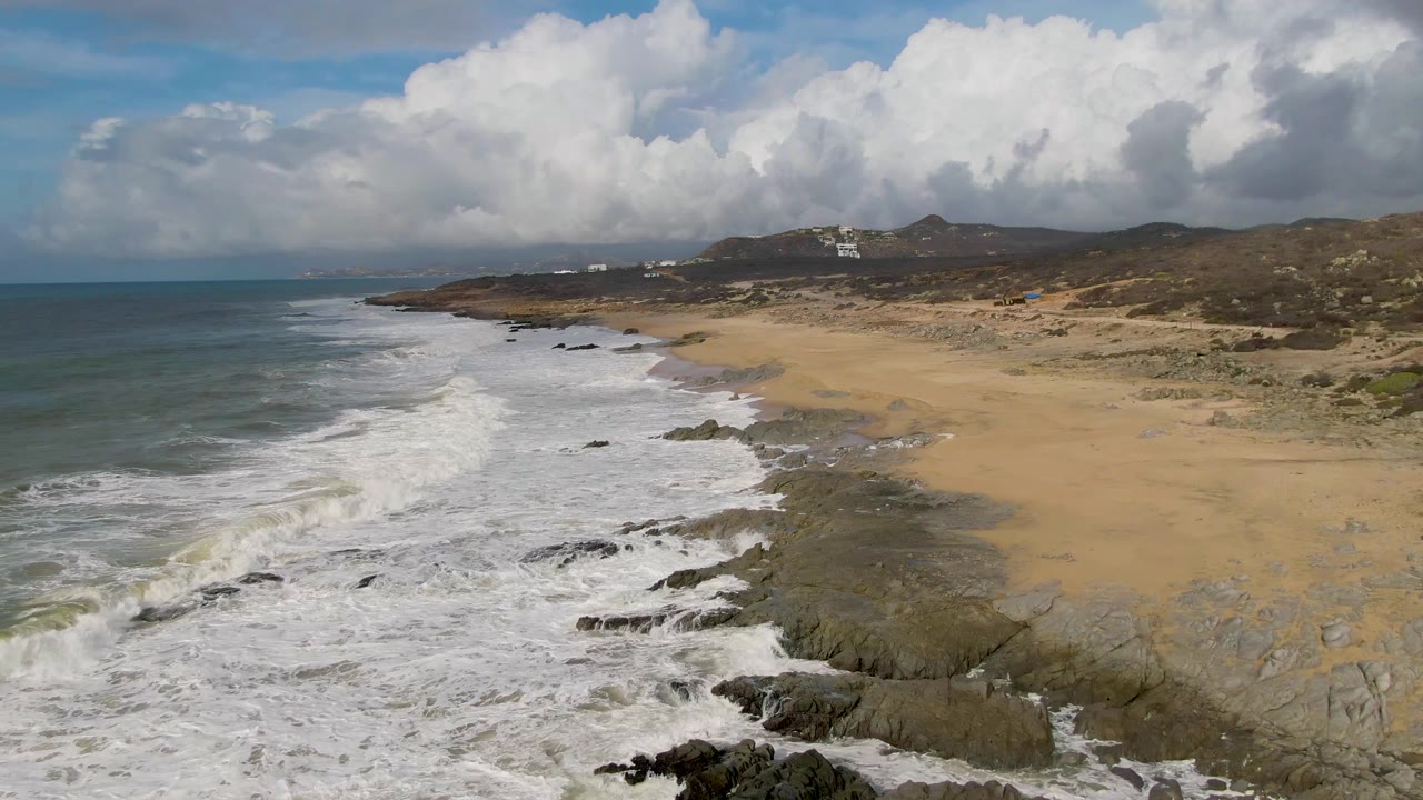 Foamy surf spreads across rocks beside a wide tan beach.