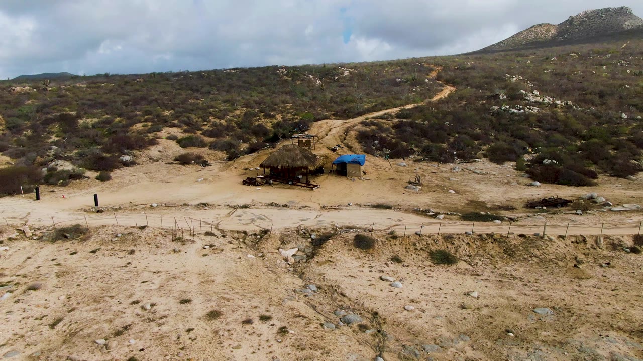 A slightly later view shows the winding dirt track leading uphill through sparse Punta Gorda vegetation, with the shelter and blue cover near the lower center and no visible people.