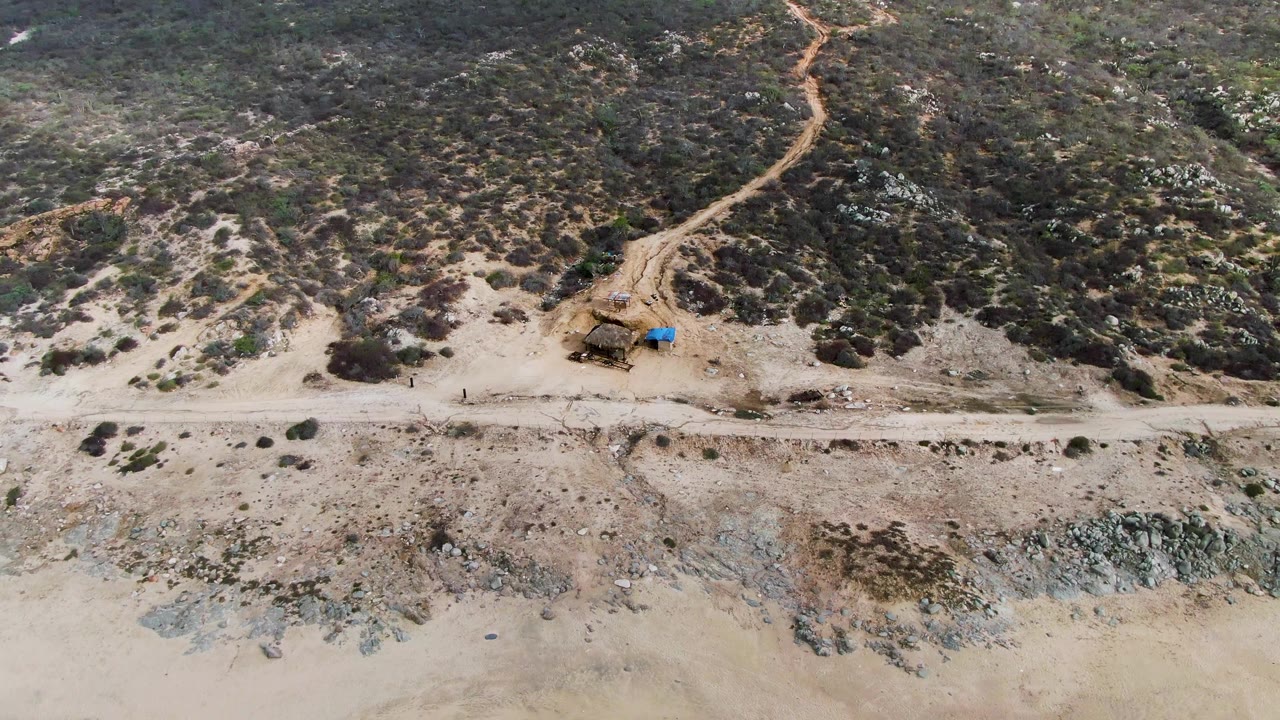 Aerial coastal road and scrub hillside above a sandy beach.