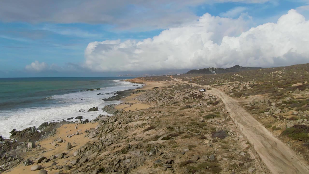 Elevated view of a dirt road beside rocky coast and ocean surf.
