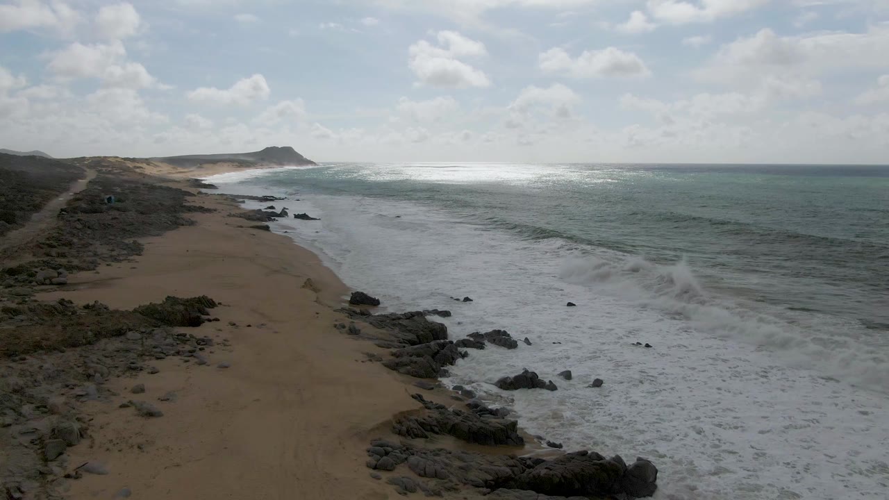 Aerial view of waves breaking along a sandy beach with rocky shoreline.