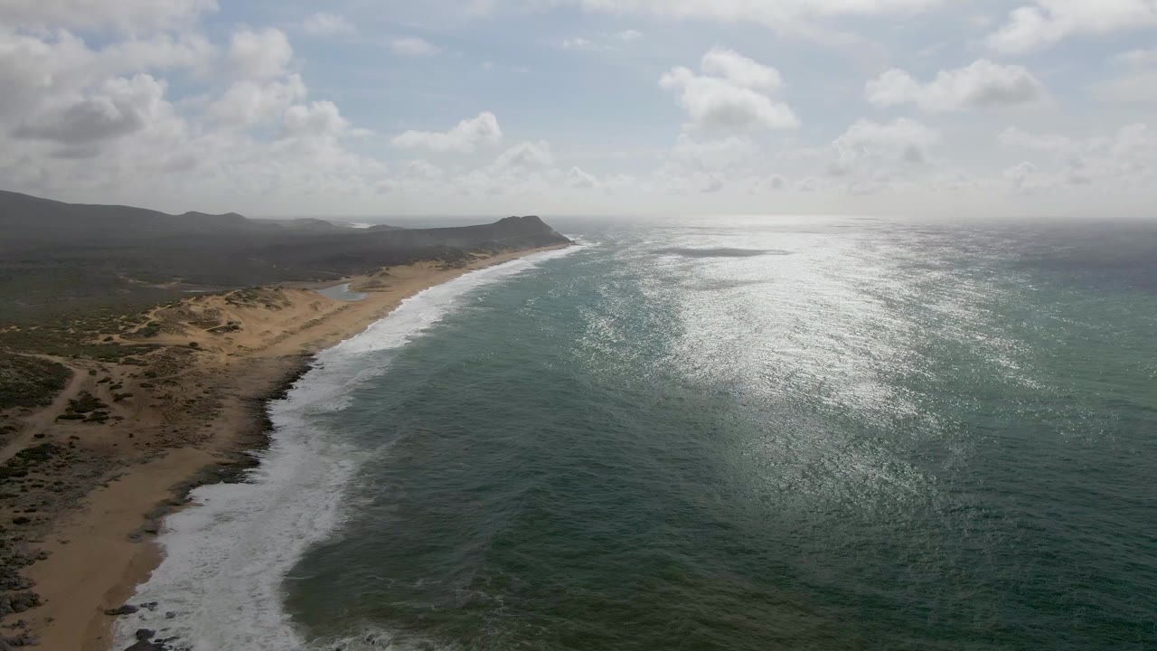 Aerial shoreline with surf band, dunes, and distant headland