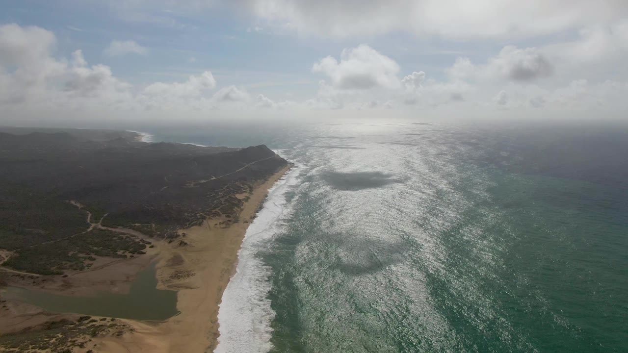 Midway through the clip, the Punta Gorda shoreline remains framed from above with lagoon water in the lower left, white waves along the sand, and no visible people.